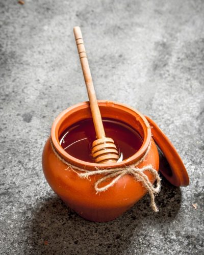 Fresh honey in a clay pot with a wooden spoon. On rustic background.
